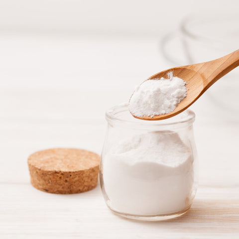 Natural baking soda powder in a glass jar with wooden spoon, commonly used in DIY skincare for gentle exfoliation, deep cleansing, and balancing skin.